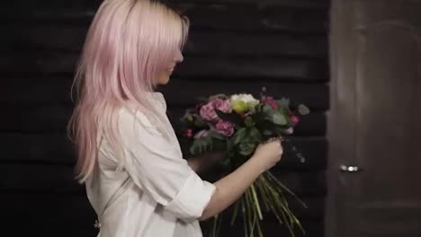 A-pink-haired-young-woman-makes-the-design-of-the-bouquet,-complementing-the-composition-with-willow-branches.-Smiling.-Dark-background