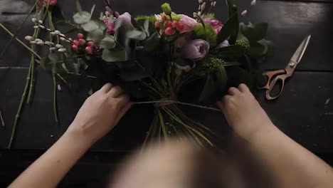 A-beautiful-bouquet-of-flowers-decorated-by-a-florist-lies-on-a-table.-The-girl-tightly-tightens-it-with-rope-on-the-stems.-View-from-above