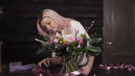 Professional-girl-florist-binds-the-bottom-of-the-bouquet-with-silk-pink-ribbons.-Dark-studio.-Slow-motion