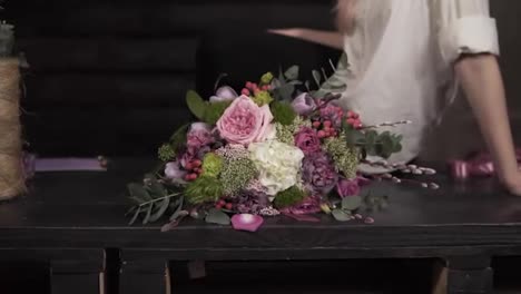 Stunning-slow-motion-footage-of-an-attractive-delicate-young-woman.-She-is-sitting-on-the-table-with-gorgeous-bouquet-next-to-her.-Throwing-a-handful-of-petals-to-the-camera