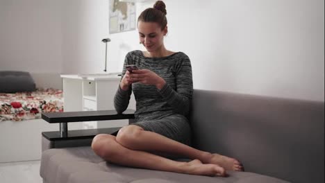 Round-camera-movement:-smiling-young-woman-sitting-on-the-couch-at-home-looking-at-phone-and-typing-a-message