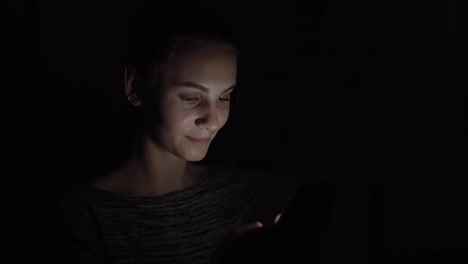 Closeup-view-of-a-woman-using-her-phone-in-a-dark-room,-chatting-in-the-darkness-with-smartphone,-communicating-with-friends-online