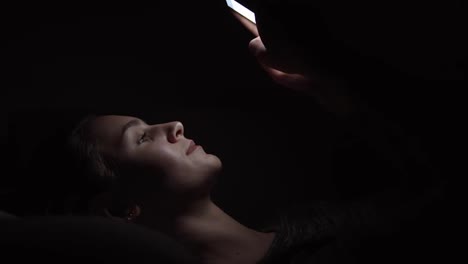 Closeup-view-of-a-woman-laying-on-a-couch-and-using-her-phone-in-a-dark-room,-chatting-in-the-darkness-with-smartphone,-communicating-with-friends-online