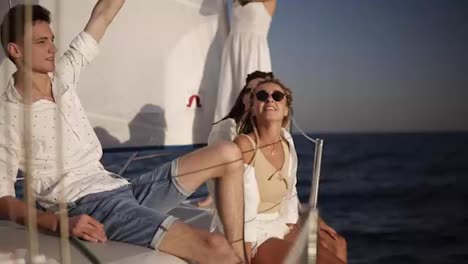 Four-friends-having-relaxing-cruise-on-the-yacht.-They-sitting-on-the-ship-board-and-enjoying-the-moment---guy-waving-the-balloones,-celebating.-Slow-motion