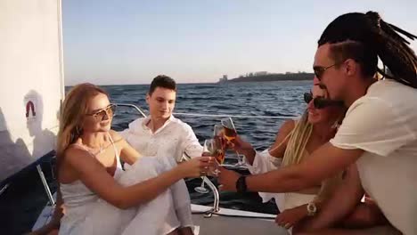 Friends-spend-a-weekend-on-a-yacht.-Event-on-the-yacht.-Merry-company-is-celebrating-a-birthday-on-a-yacht.-Group-of-four-are-clinking-with-the-champange-glasses-and-smilling
