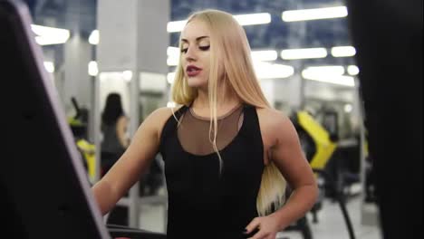 Young-attractive-blond-caucasian-woman-with-piercing-in-black-sport-outfit-breathing-intensly-while-jogging-on-treadmill-simulator-in-slomo