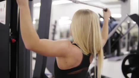Attractive-young-blond-caucasian-woman-with-sporty-body-training-hard-on-a-lat-pull-down-mashine-at-the-gym.-Healthy-lifestyle-concept.