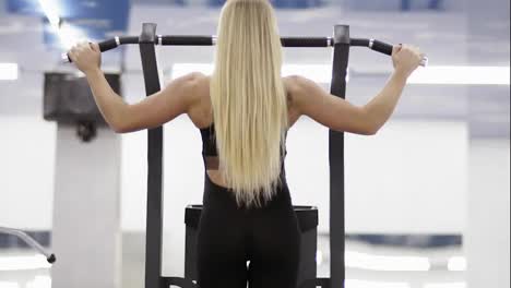 Strong-female-bodybuilder-with-blond-hair-with-muscular-arms-performing-pulls-up-on-a-horizontal-bar-at-the-gym.-Backside-footage