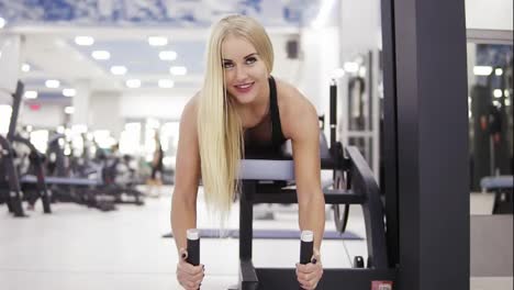 Frontside-footage-of-beautiful-muscular-girl-smiling-while-performing-exersices-on-leg-curl-mashine-set-at-the-gym.-Building-strong-core.-Fitness-and-healthcare.