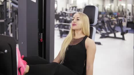 Attractive-young-blond-caucasian-woman-with-sporty-body-smiling-while-exercising-on-horizontal-leg-press-at-the-gym.-Healthy-lifestyle-concept.
