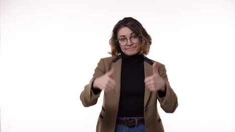 Young-caucasian-woman-wearing-black-blazer-and-brown-jacket-strictly-gesturing-with-thumb-up-YES,-then-showing-hands-shape-meaning-denial-saying-NO-then-smiling-and-over-again.-Standing-over-white-background-at-studio