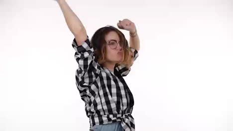 Young-woman-in-plaid-shirt-listening-to-music-using-headphones-standing-over-isolated-white-background-very-happy-and-excited-doing-dance-with-arms-raised,-emotionally-moves.-Slow-motion
