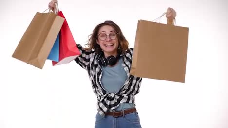 Cheerful-beautiful-european-young-woman-in-glasses-and-headphones-on-neck-holding-colorful-shopping-bags-in-season-sale,-happily-shakes-them-isolated-on-white-background