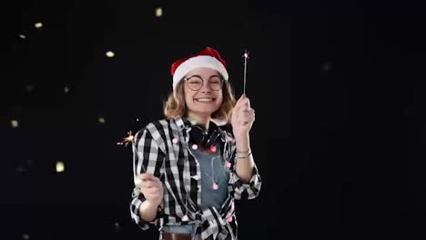 A-cute-woman-in-Santa-hat-and-colorful-garlands-and-headphones-on-neck-with-two-sparklers-dance-at-Christmas-night-party-over-black-background.-Smiling,-cheerful-young-woman-having-fun