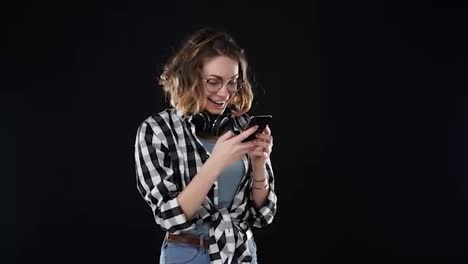 European-stylish-young-woman-receiving-good-news-while-reading-from-the-screen-on-mobile-phone-isolated-over-black-background-and-got-super-excited.-Emotions-concept