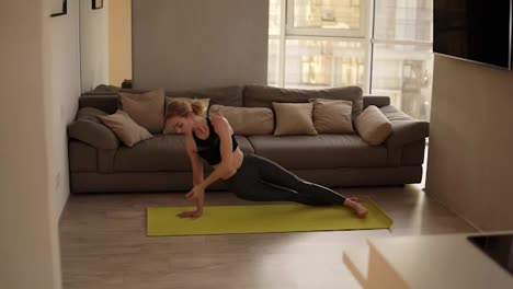 Woman-exercising-at-home-practicing-various-yoga-asanas,-doing-downward-facing-dog-pose-in-living-room-on-a-yellow-training-mat.-Slow-motion