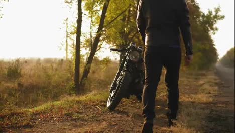 Back-view-of-a-man-in-helmet-and-leather-jacket-coming-up-to-his-bike-and-starting-the-engine-while-standing-on-the-roadside-in-a-sunny-day-in-autumn
