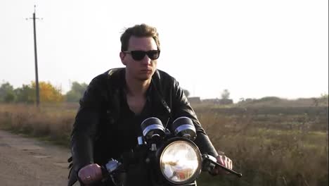 Closeup-view-of-a-stylish-cool-young-man-in-sunglasses-and-leather-jacket-riding-motorcycle-on-a-asphalt-road-on-a-sunny-day