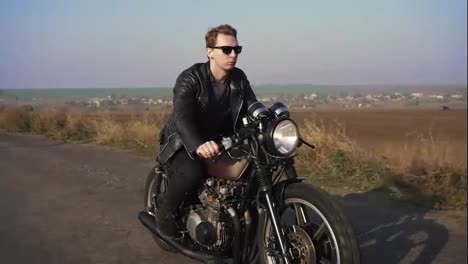Side-view-of-a-stylish-cool-young-man-in-sunglasses-and-leather-jacket-driving-his-chopper-on-a-asphalt-road-on-a-sunny-day.-Shot-in-4k