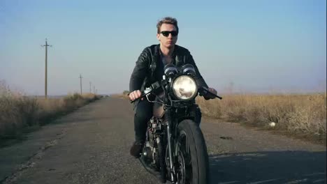Closeup-view-of-a-stylish-cool-young-man-in-sunglasses-and-leather-jacket-riding-motorcycle-on-a-road-on-a-sunny-day.-Then-the-camera-moves-forward-and-the-man-visibly-shrinking-into-the-distance