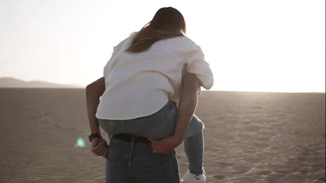 Happy-and-cute-adorable-adult-couple-in-white-shirts-and-jeans-man-with-woman-girlfriend-on-piggy-back,-have-fun-play,-laugh,smile-on-sunset-at-desert-crazy-in-love,-emotions-and-relationship