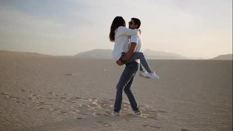 Perfect-scene-of-young-couple-in-empty-desert.-man-holding-her-woman-on-arms-and-turning-her-around,-have-fun-emotionally,-laugh,smile-on-sunset-at-desert-crazy-in-love,-emotions-and-relationship.-Slow-motion