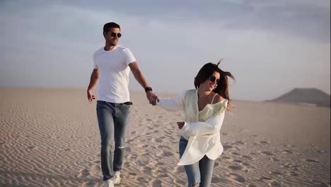 Couple-holding-hands-running-having-fun-under-sun-in-playful-and-romantic-relationship-under-sun-and-blue-sky-in-desert.-Two-young-lovers-cheerful-together-on-romance-in-summer.-Wearing-casual-clothes