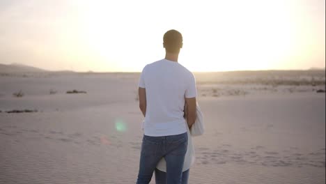 Young-couple-standing-and-hugging,-man-holding-her-woman-from-the-back-on-the-dried,-sandy-desert-watching-the-landscape-together-thoughtfully.-Overview-footage.-Lens-flares