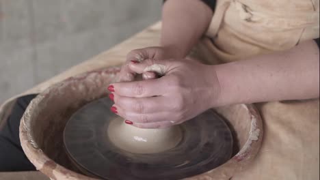 Close-up-of-potter's-hands-with-red-manicure-working-with-wet-clay-on-a-pottery-wheel-making-a-clay-product-in-a-workshop.-Unrecognizable-female-person