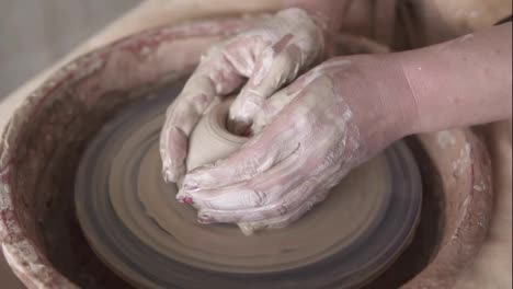 Close-up-of-potter's-hands-with-red-manicure-working-with-wet-clay-on-a-pottery-wheel-making-a-clay-product-in-a-workshop.-Unrecognizable-female-person.-Slow-motion
