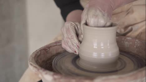 Female-potter's-hands-with-red-manicure-working-with-wet-clay-on-a-pottery-wheel-making-a-clay-product-in-a-workshop.-Unrecognizable-female-person-forming-a-vase,-pulls-it-up