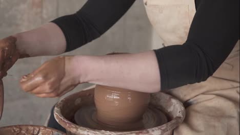 Female-potter-cuts-off-excess-clay-on-the-top-of-the-vase.-Creating-vase-of-clay-close-up.-Girl-makes-cup-out-of-clay-closeup.-Twisted-potter's-wheel.-Women's-hands-making-clay-vase