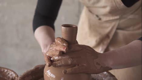 Female-potter's-hands-with-red-manicure-working-with-wet-clay-on-a-pottery-wheel-making-a-clay-product-in-a-workshop.-Unrecognizable-female-person-forming-a-vase,-pulls-up-the-neck
