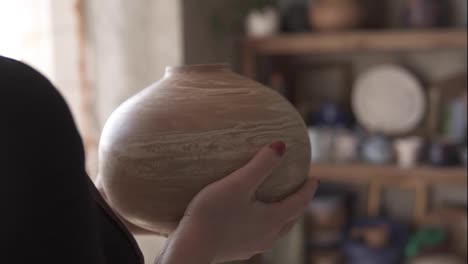 Close-up-footage-of-female-potter-putting-handmade-vase-on-shelf-in-studio,-pleased-with-her-work,-smiling-to-the-camera.-Slow-motion