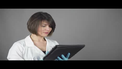 Female-doctor-in-blue-rubber-gloves-using-a-tablet-isolated-on-grey-background.-Healthcare-concept.-Shot-in-4k.