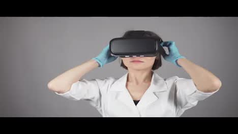 Feale-doctor-conducting-experimental-medical-procedure-wearing-virtual-reality-headset-isolated-on-grey-background.-Modetn-healthcare-concept.-Shot-in-4k