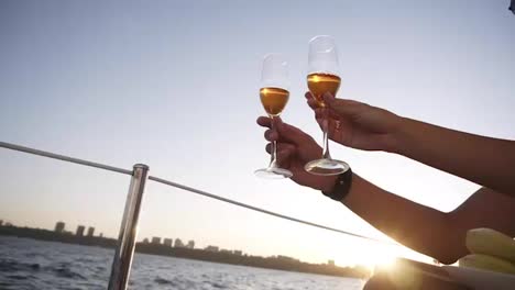 Two-crystal-glasses-with-wine-or-champagne-on-background-of-sea,-sunlight-and-blue-sky.-Man-and-woman-are-holding-their-and-clinking-by-them,-luxury-celebration-on-the-yacht