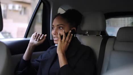 Beautiful-Afro-American-businesswoman-sitting-on-the-backseat-of-a-taxi-with-bright-leather-salon,-talking-by-her-mobile-phone.-Relaxed-woman-talking-by-phone-in-the-car.-Slow-motion
