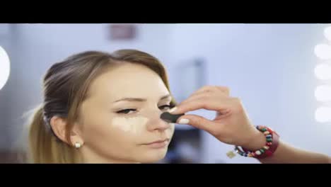 Closeup-of-professional-makeup-artist-applying-concealer-to-skin-of-young-woman-with-brush-to-cover-dark-circles-and-make-face-look-brighter.-Shot-in-4k