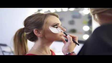 Makeup-artist-applying-eyeshadow-on-eyelid-using-makeup-brush-and-protecting-sking-with-white-patches.-Professional-makeup.-Shot-in-4k