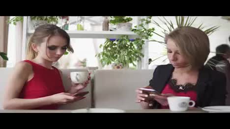 Two-young-girlfriends-using-smartphone-and-talking-in-cafe-and-drinking-coffee.-Shot-in-4k