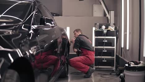 Polishing-car-with-polish-mashine.-Worker-in-red-suit-cleaning-a-black-expensive-car.