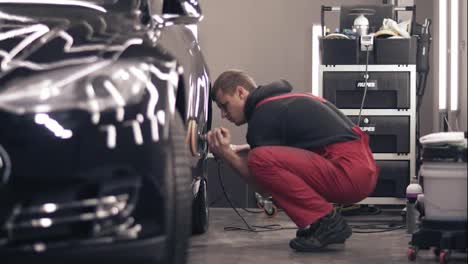 Polishing-car-with-polish-mashine.-Worker-in-red-suit-cleaning-a-black-expensive-car.
