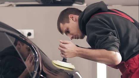 Male-worker-at-autocenter-polishing-black-new-car-with-precise-accuracy.