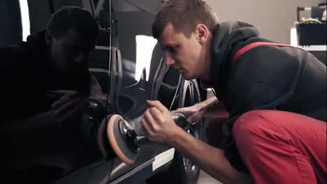 Process-of-polishing-black-newcar-with-professional-mashine.-Man-in-red-onepiece-worksuit-working-hard.