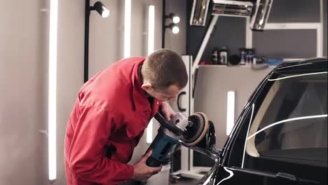 Man-in-red-worksuit-polishing-rear-view-mirror-of-a-black-new-car.