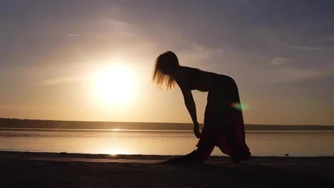Die-Silhouette-Einer-Fitten-Frau-Am-Wasser-Entfaltet-Die-Yogamatte-Und-Bereitet-Sich-Auf-Yoga-Oder-Pilates-Vor.-Sonnenuntergang-Am-Strand