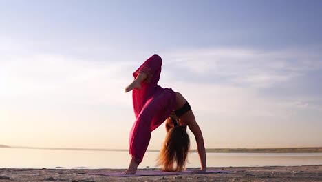 Close-up-view-of-a-young-woman-in-pink-yogi-pants-practicing-on-sand-near-the-sea-or-lake-in-the-morning.-Posture---Urdhva-dhanurasana