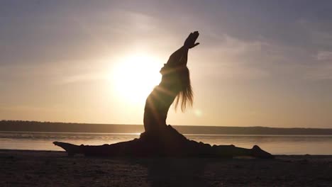 Silhouette-of-a-beautiful-yoga-girl-at-sunrise-on-the-beach.-Hanumanasana,-monkey-pose.-Sunrays-lay-on-a-body