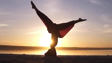 Sporty-beautiful-young-advanced-yoga-woman-standing-in-Sirsasana-outdoors-on-the-beach.-Beautiful-sunset,-silhouette